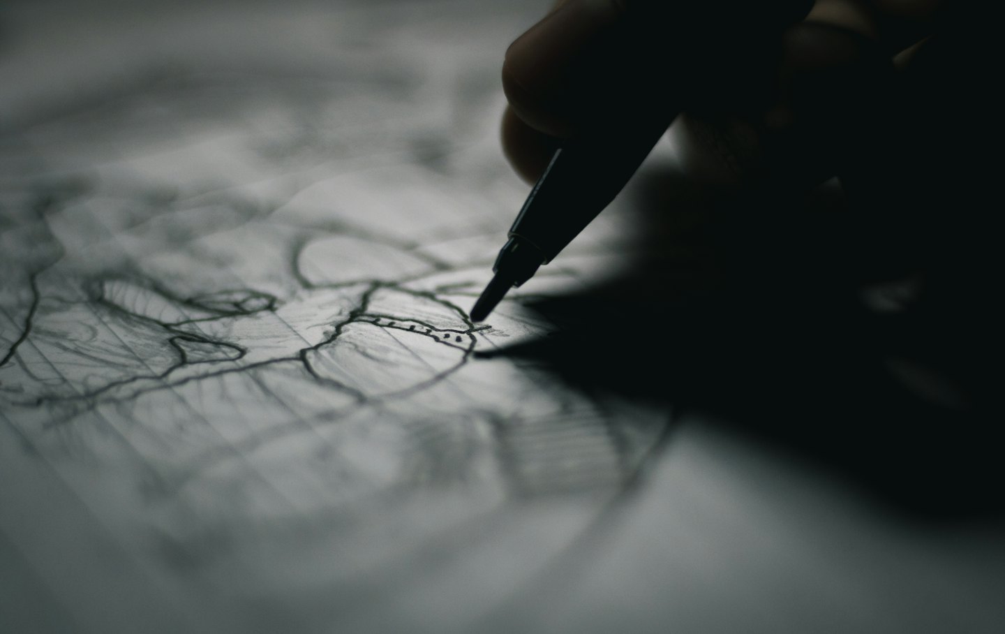 A hand uses a fine-tip pen to draw lines on paper.