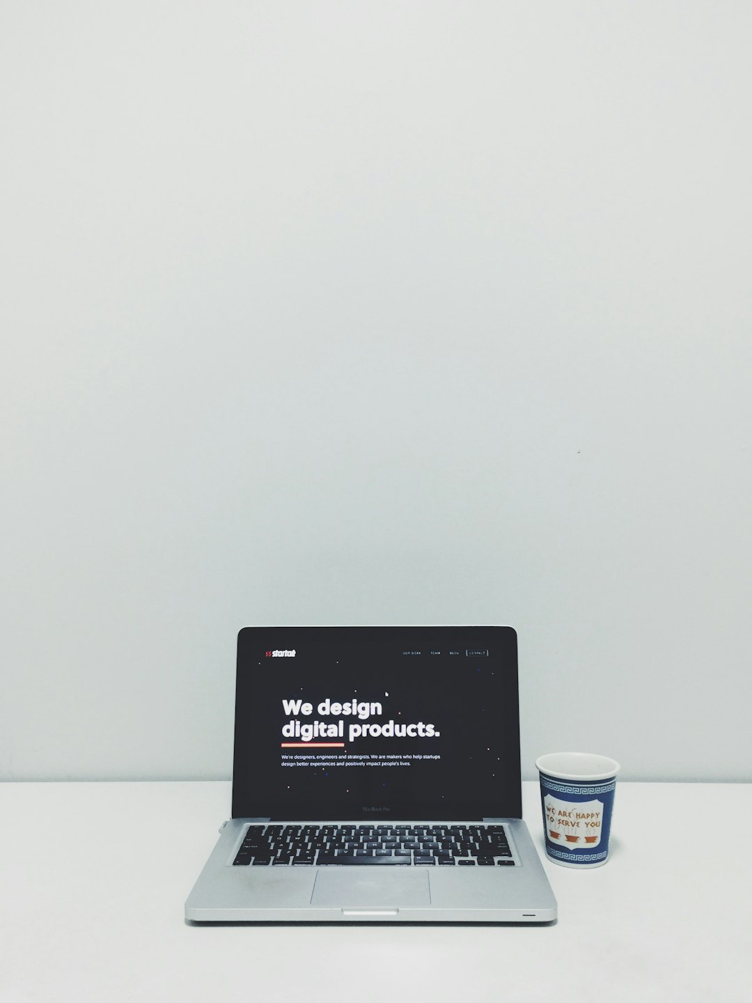 Silver laptop displays 'We design digital products' on a white desk.