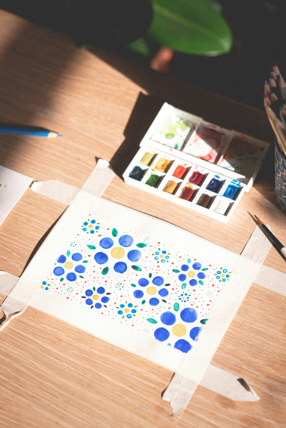 Watercolor art supplies on a wooden desk with natural light.